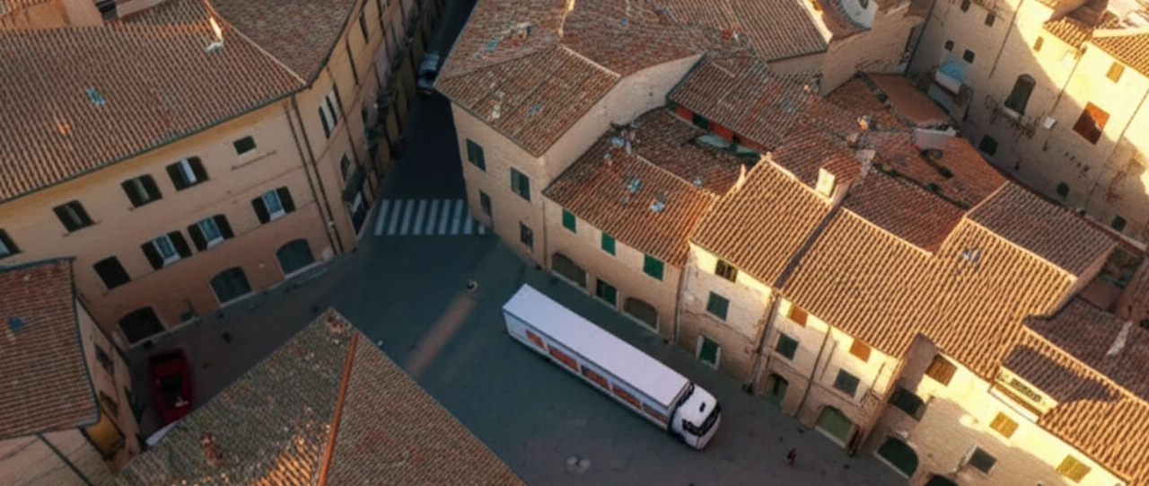 Vista aerea di un moderno camion per traslochi in una piazza storica di una pittoresca città italiana, con tetti in terracotta e strade acciottolate.