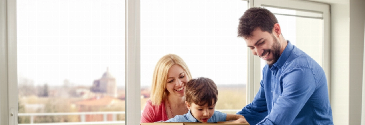 Famiglia caucasica che disimballa felicemente la prima scatola nel loro nuovo soggiorno illuminato dal sole, con vista su un quartiere italiano.