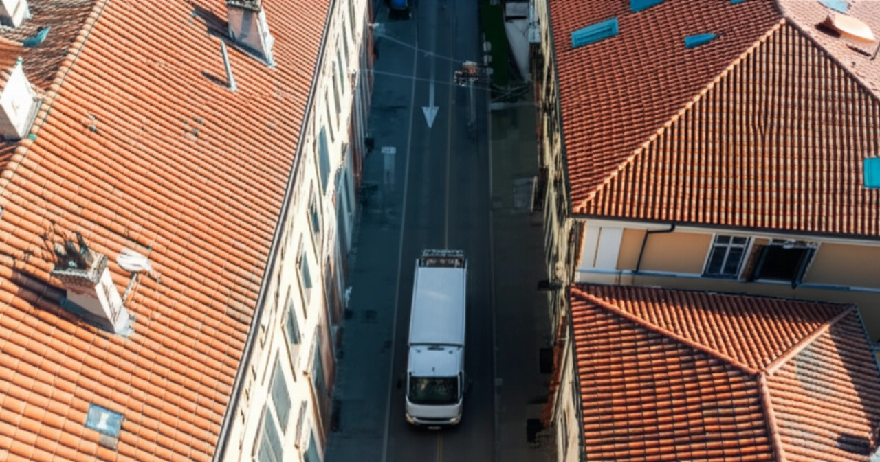 Vista aerea iperrealistica di un camion di traslochi moderno parcheggiato in una strada di città piemontese, con edifici storici.