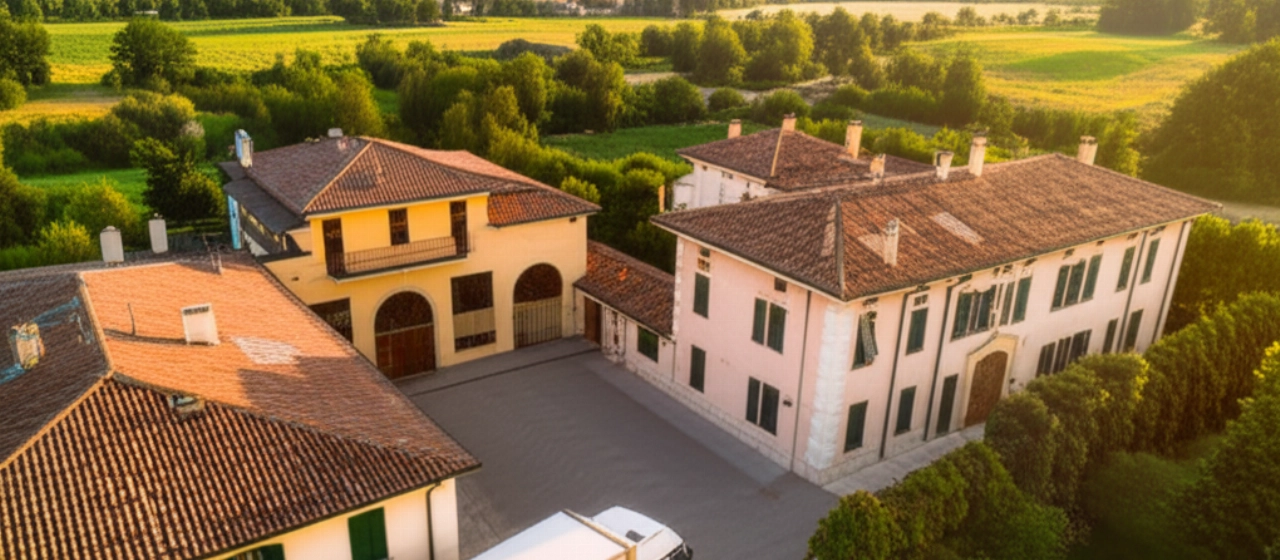 Vista aerea iperrealistica di un camion di traslochi parcheggiato davanti a un edificio residenziale italiano con tetti in terracotta, in una tranquilla zona suburbana al tramonto.